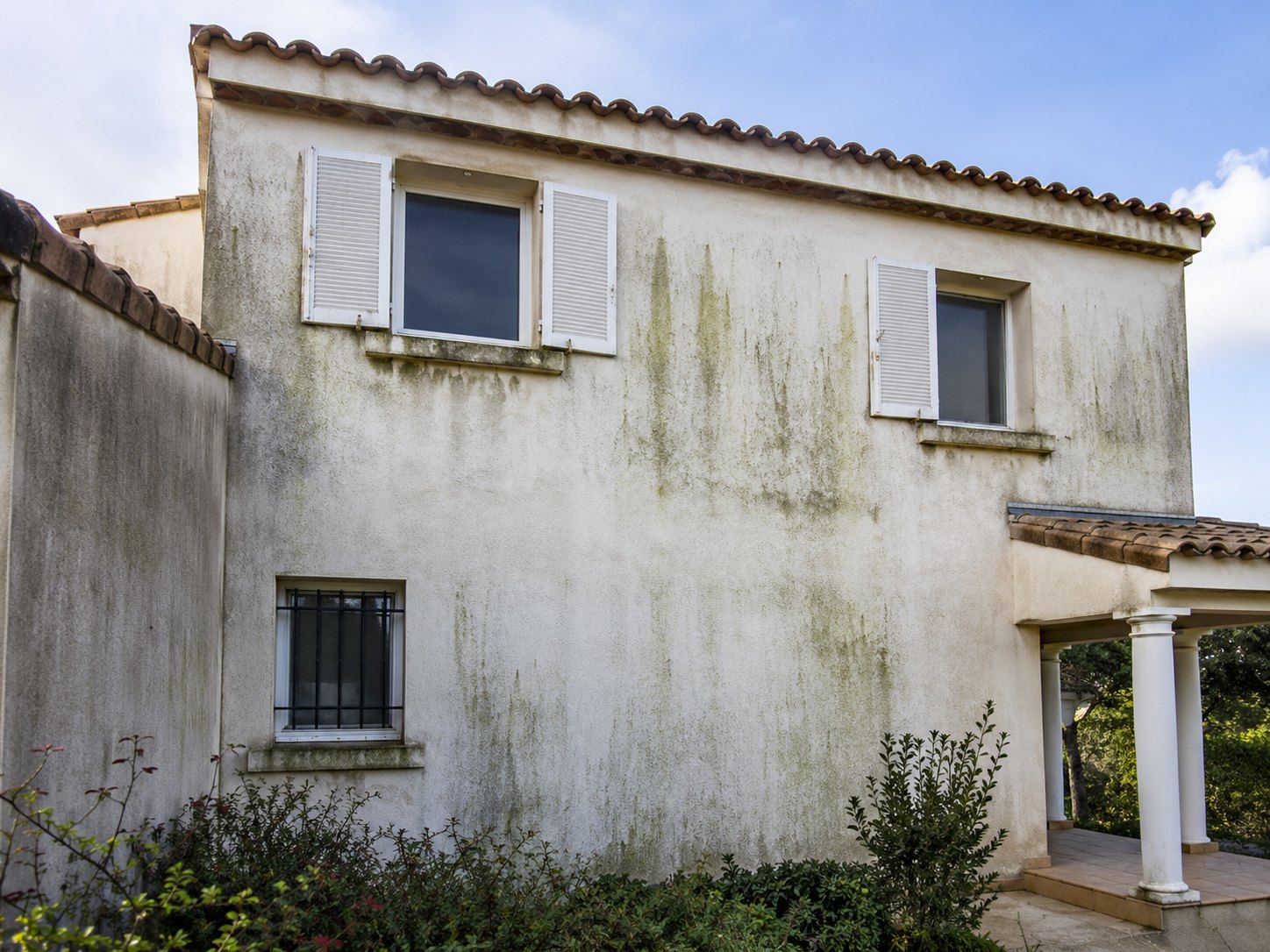 Façade enduite marquée par des salissures et des coulures vertes, photographie d’illustration